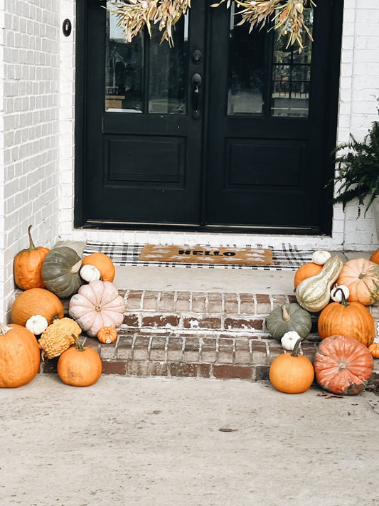 Decorative pumpkins and gourds on a front porch with a black door.